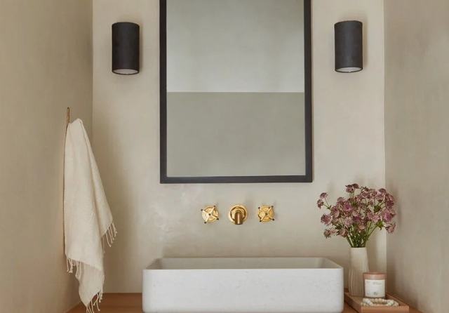 Microcement wall behind a stone basin and brass taps